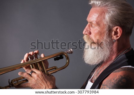 PIcture of a white haired trumpet player with a long white beard. Profile picture with side light.