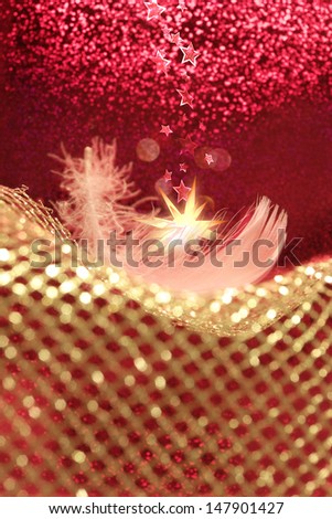 christmas decoration arrangement of a white feather, softly lying on a golden net with stars falling from above