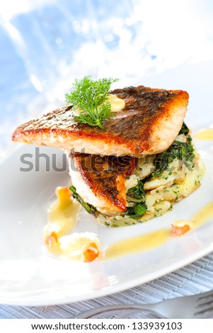 Beautifully styled mediterranean salmon dish on white plate in an expensive restaurant setting.  Shallow depth of field.