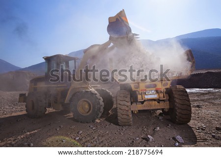 Construction vehicles on building site with dust filled air and blue mountains background