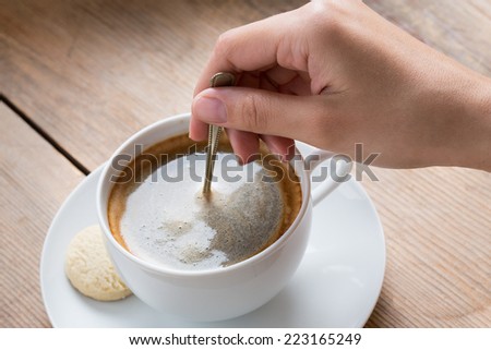 Cup of coffee with foam being stirred by a human hand
