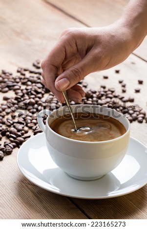 Cup of coffee with foam being stirred by a human hand