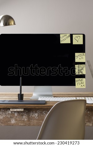 Computer screen and keyboard and mouse on a wood table with white wall with sticky notes on screen