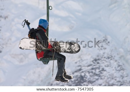 person with snowboard moving up on chair lift