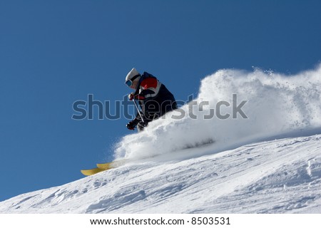 skier in clouds of snow powder against a blue sky