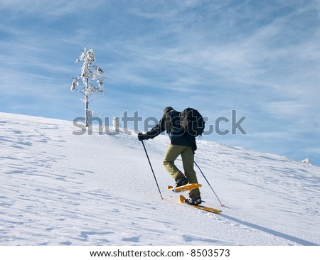 backpacker moving up in winter mountain under blue sky