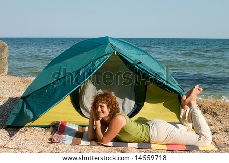 Smniling girl lie near of her tent at seaside