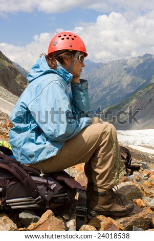 mountaineer girl sitting on backpack and looking to mountains