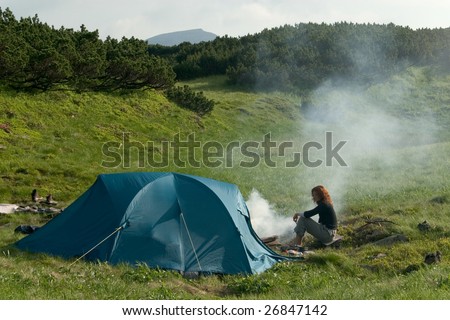 Girl siting near of a tent and making a campfire