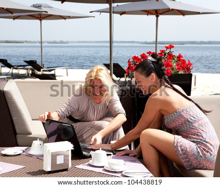 Two women in coffee look in netbook and smile