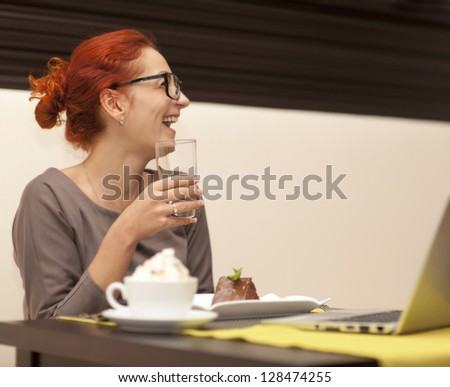 Businesswoman sitting at table in cafe using notebook. Iced coffee stands in the foreground
