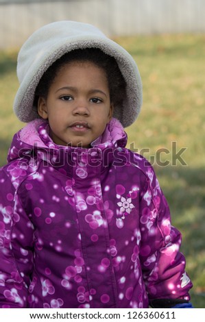 An young African-American girl wearing a winter coat and a hat.