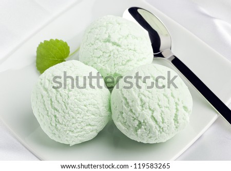 three balls of peppermint ice cream on a plate with spoon and mint leaf