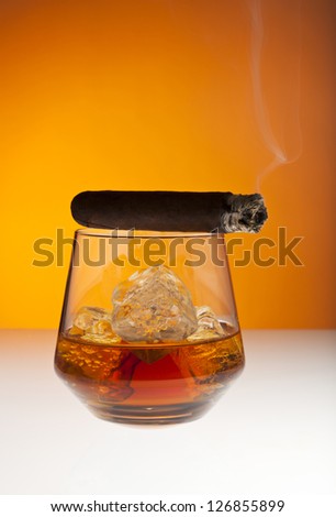 Smoking cigar on top of tumbler filled with whisky on the rocks