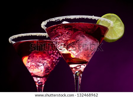 Closeup of pink cocktails in martini glasses with sugared edges, ice cubes and lime slices