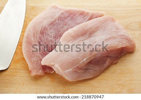 Two slices of raw turkey meat on wooden chopping board