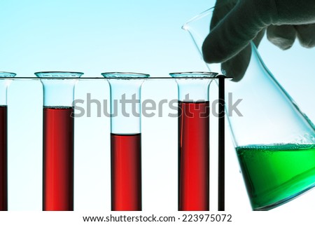 Chemical laboratory concept. Hand in glove with Erlenmeyer flask behind rack of test tubes, blue light