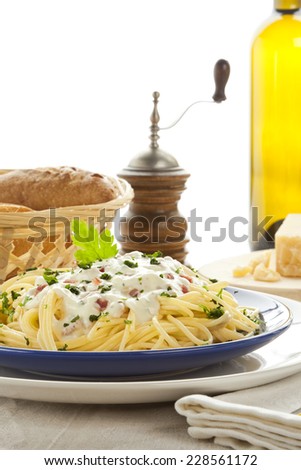 Spaghetti Carbonara pasta, wine bottle, pepper mill, Parmesan Cheese and bread in background