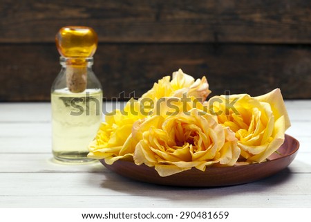 Yellow rose blossoms in wooden bowl, fragrance bottle in back