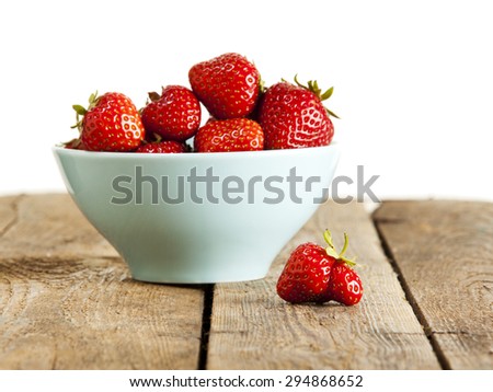 Misshaped strawberry in front of bowl with perfect fruit on wooden crate, white background