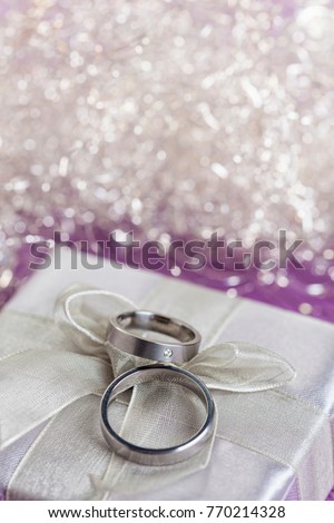 Pair of wedding rings on top of silver gift box with bow, bokeh in background