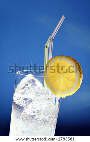 top of slanting glass filled with clear liquid, ice cubes, straws and lemon slice