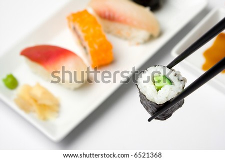 kappamaki held between chopsticks, various sushi on a plate in  background