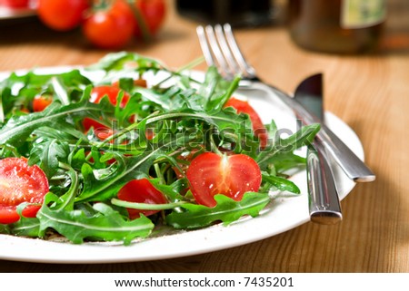 italian salad from tomatoes, rucola, grated parmesan cheese, pepper, vinegar, olive oil on white plate, arranged with cutlery, oil and vinegar bottles, cherry tomatoes on wooden table