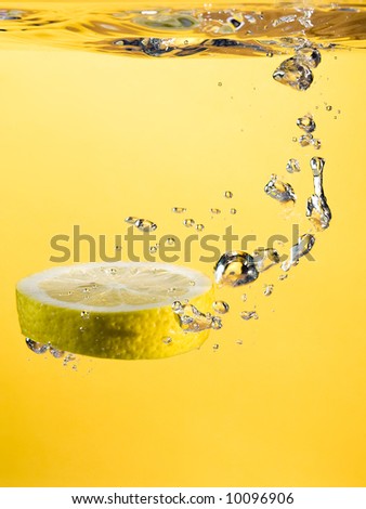 lemon slice diving into clear liquid, yellow background
