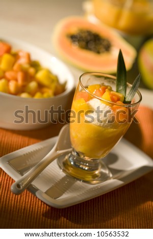 dessert with icecream and tropical fruit in glass cup, chopped and halved fruit in background