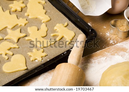 christmas cookies cut out of dough on baking board with utensils, ingredients