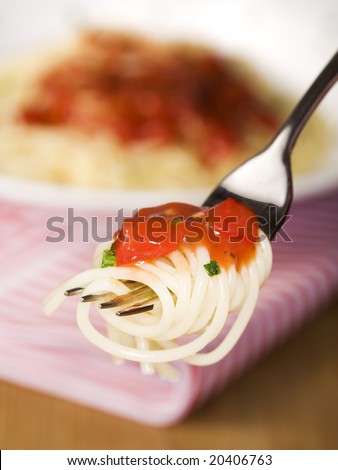 spaghetti pasta curled on a fork, topped with tomato sauce, pasta dish in background