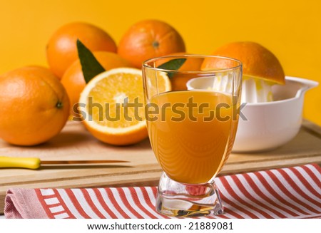 glass of freshly squeezed orange juice on kitchen towel, fruits, knife, citrus squeezer in background