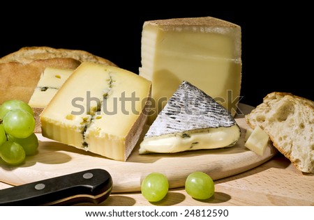 three kinds of cheese arranged on a platter with grapes, bread, knife