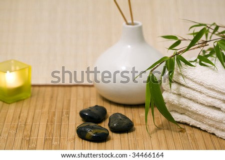 candle, incense sticks in vase, towels, hot stones, bamboo branch on bamboo mat