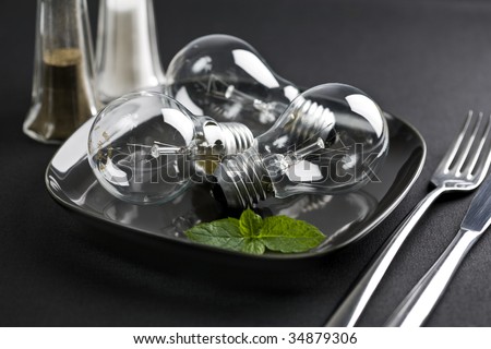 clear light bulbs on plate, garnished with mint leaves, salt and pepper dispenser, cutlery, on black table cloth