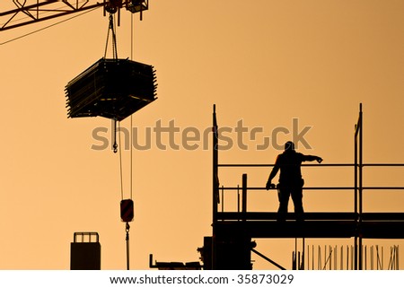 silhouette of construction worker on a frame directing a crane with heavy load