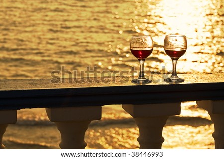 two glasses of red wine standing in golden sunset light on handrail of balcony at the sea