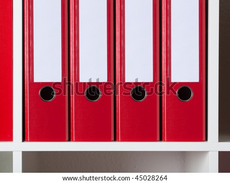 four red ring binders with blank labels on a rack