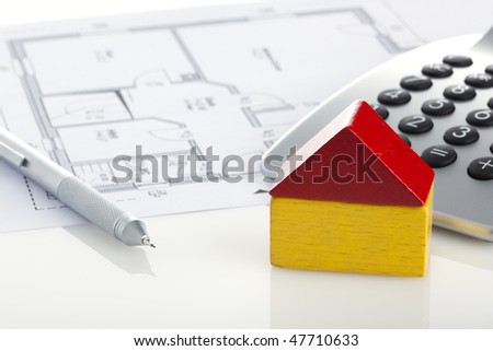 mechanical pencil, toy block house and calculator on blueprint of floor plan, closeup