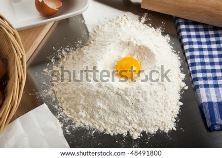 home baking scene - heart shaped heap of flour with egg yolk on top, surrounded by ingredients and utensils