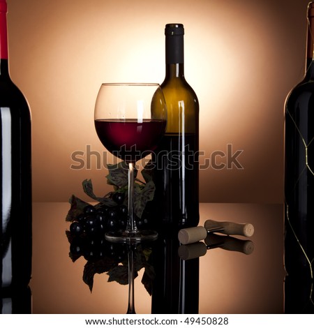 glass of red wine with opened bottle and black grapes, framed by two more wine bottles