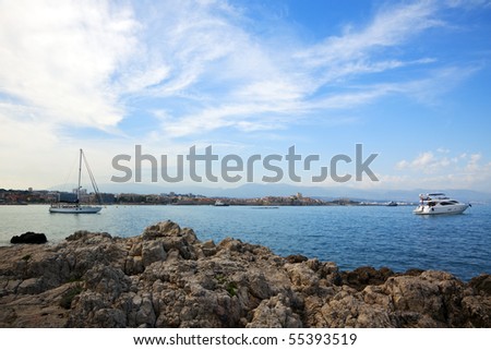 Antibes at the Côte d\'Azu, seen from Cap d\'Antibes, small yacht and sailboat anchored in the bay, rocks in foreground