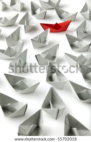 single red paper boat between lots of gray paper boats
