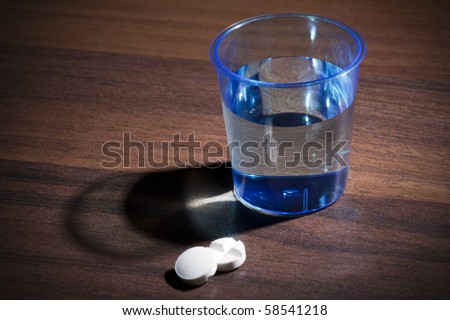 two migraine pills and a plastic cup of water on a table, focus on the cup