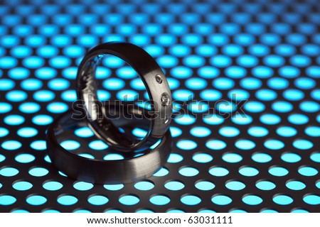 silver or titanium wedding rings on perforated sheet metal in blue light