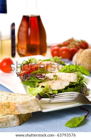 three threads of grilled chicken fillet on fresh green garden salad with tomatoes and bread with herbs, oil and vinegar bottles in background