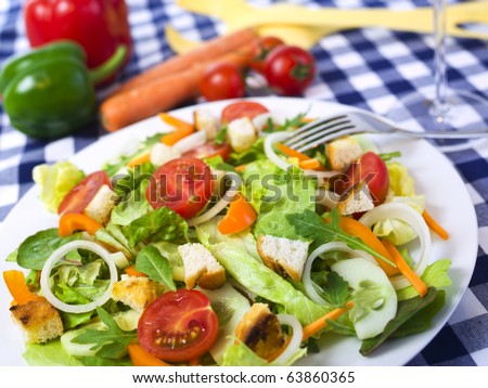 healthy garden salad with tomatoes, orange bell pepper, onions, lettuce, croutons, cucumber slices, on dining table