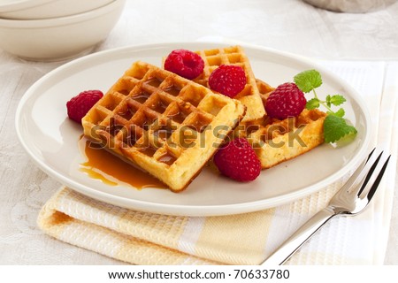 belgian waffles with syrup or caramel sauce served on a plate, garnished with raspberries and mint