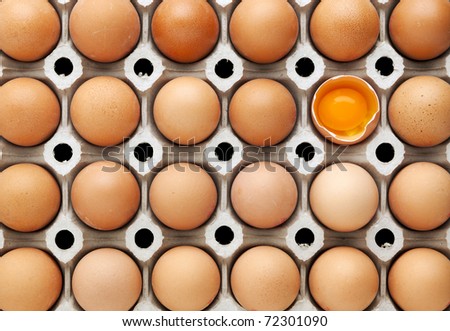 cardboard tray filled with brown eggs, one egg is broken